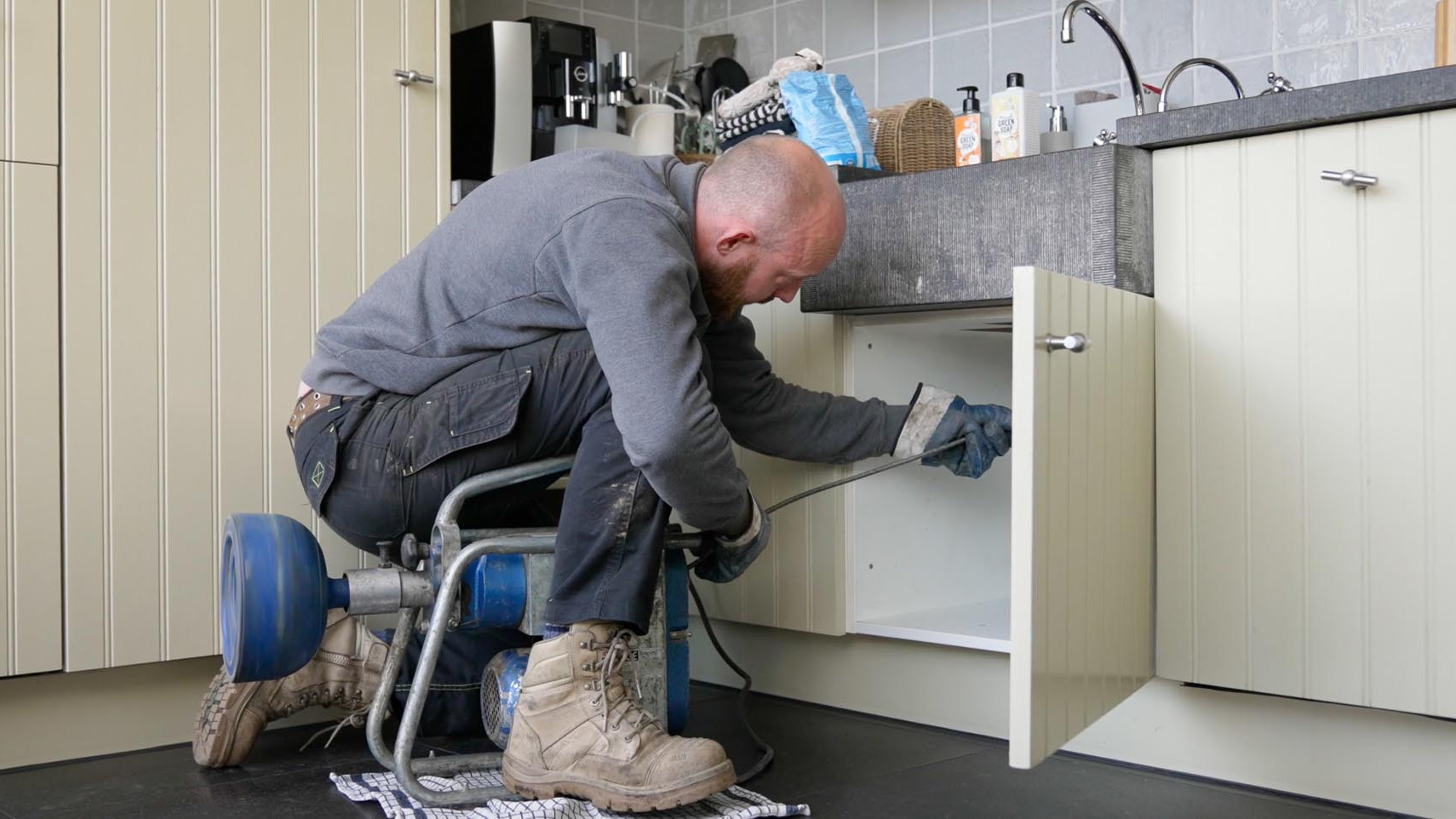 Medewerker ontstopt een verstopte gootsteenafvoer met een ontstoppingsmachine