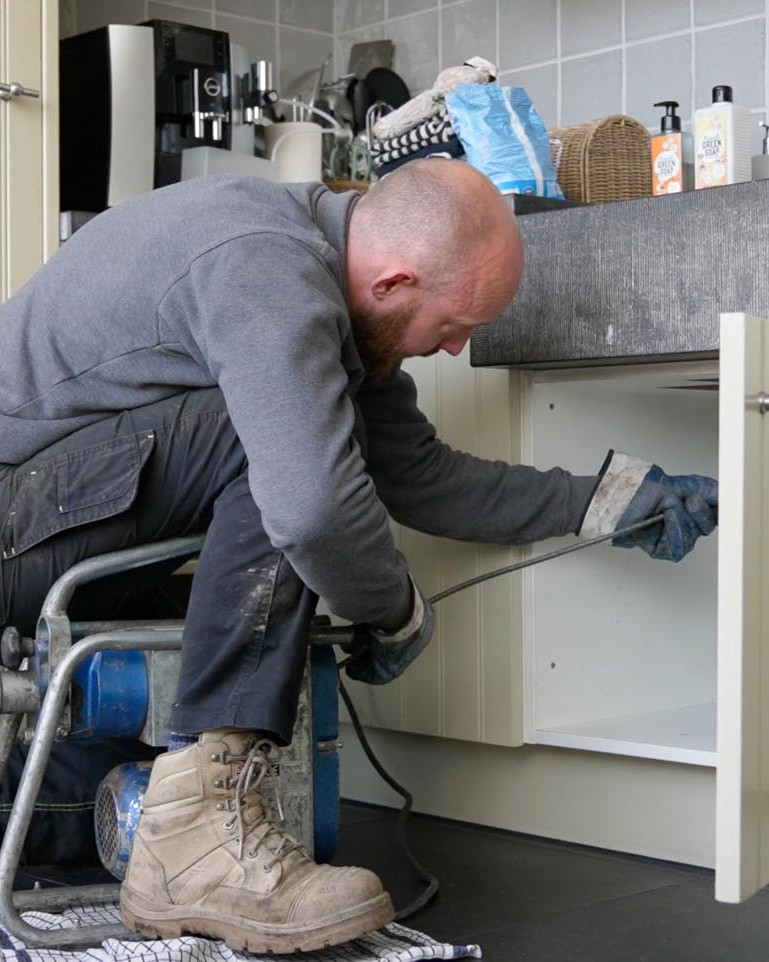 Medewerker ontstopt een verstopte gootsteenafvoer met een ontstoppingsmachine